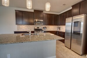 A modern kitchen with dark wood cabinets, stainless steel appliances, granite countertops, and pendant lighting. - Romantic 3-BR Townhouse With Backyard ~ Double Story - Pet Friendly! (Rosenberg)