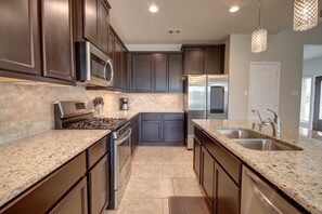 A modern kitchen with dark cabinetry, granite countertops, stainless steel appliances, and pendant lighting. - Romantic 3-BR Townhouse With Backyard ~ Double Story - Pet Friendly! (Rosenberg)