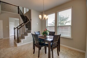 A dining area with a wooden table, four chairs, and a chandelier. A staircase with a railing is visible in the background. - Romantic 3-BR Townhouse With Backyard ~ Double Story - Pet Friendly! (Rosenberg)