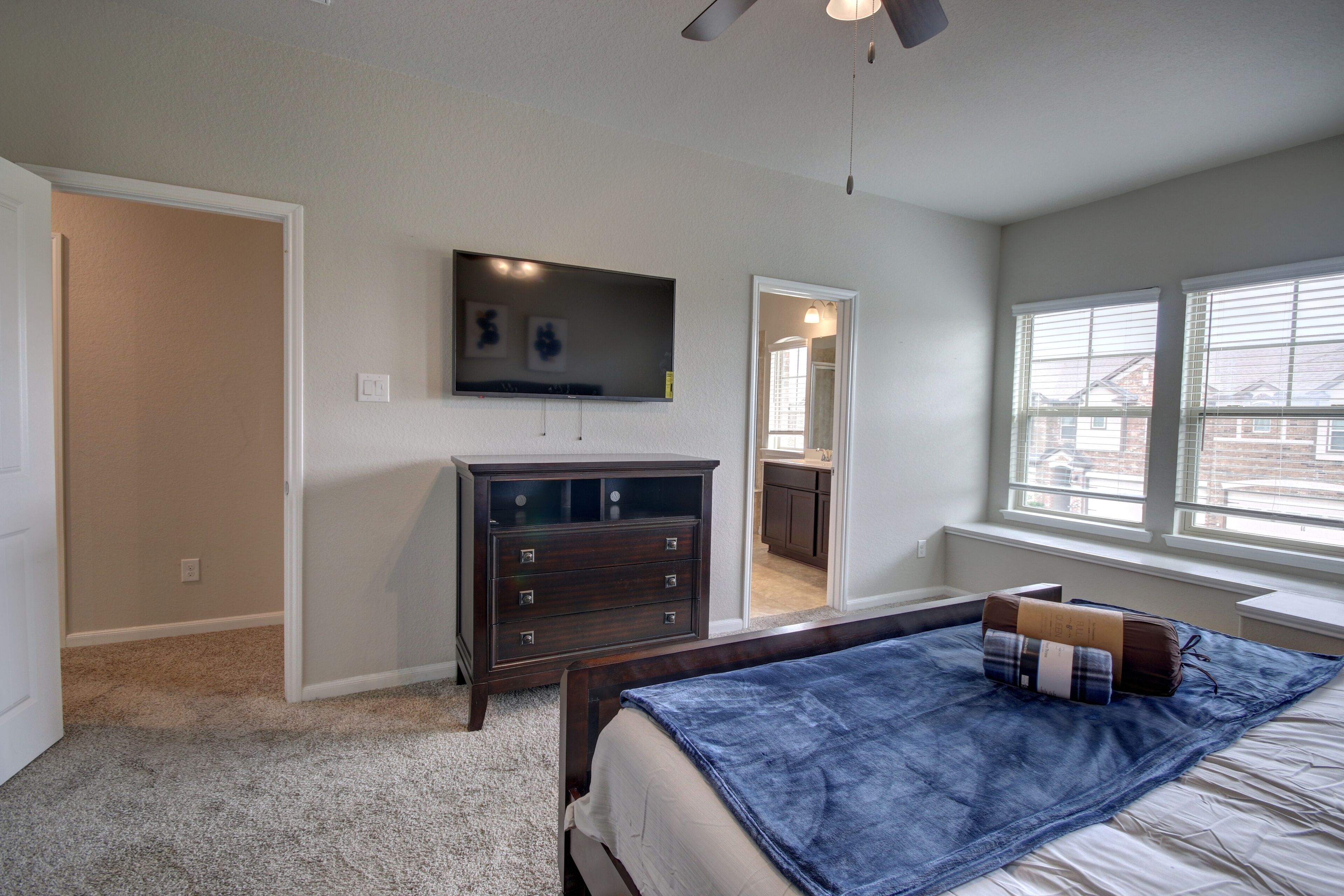 A bedroom with a bed, a dresser, a TV, and a window with blinds.