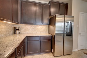 A kitchen with dark wooden cabinets, a stainless steel refrigerator, and a granite countertop. - Romantic 3-BR Townhouse With Backyard ~ Double Story - Pet Friendly! (Rosenberg)