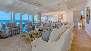 A spacious living room with a large glass door leading to a balcony, a ceiling fan, and a kitchen area visible in the background. - I'm Already There - 6 Bedroom Direct Gulf and Intracoastal with Heated Pool (Indian Shores)