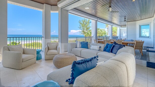 A spacious living area with a view of the ocean, featuring a large sectional sofa, a dining table, and a ceiling fan. - I'm Already There - 6 Bedroom Direct Gulf and Intracoastal with Heated Pool (Indian Shores)