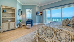 A bedroom with a large bed, a ceiling fan, a TV, and a view of the ocean through large windows. - I'm Already There - 6 Bedroom Direct Gulf and Intracoastal with Heated Pool (Indian Shores)