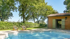 A swimming pool with two lounge chairs and a small building with a tiled roof.