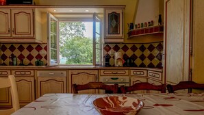 A kitchen with wooden cabinets, a dining table with a bowl, and a window with a view of trees.