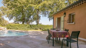 An outdoor patio with a pool, a table with chairs, and a building with a tiled roof and window with decorative bars.