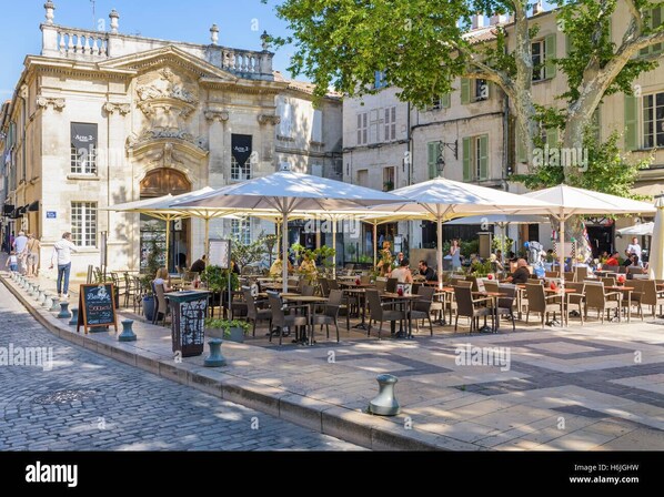 Café tables and chairs sit under umbrellas on a cobblestone street lined with historic buildings.