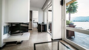 Een moderne woonkamer met een flatscreen-tv, een eethoek en een balkon met uitzicht op het water en de bergen.