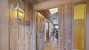 A wooden hallway with a lantern, a door with intricate patterns, and a view into another room. - 221W: Family Friendly Avalon Home, Golf Cart, Large Deck + Outdoor Dining (Avalon)