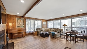 A spacious living room with a piano, a sofa set, a dining table with chairs, and large windows with sheer curtains. - 221W: Family Friendly Avalon Home, Golf Cart, Large Deck + Outdoor Dining (Avalon)