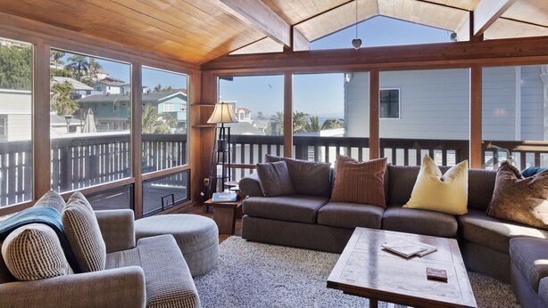 A sunlit room with a wooden ceiling, large windows, a sofa set, and a small table. - 221W: Family Friendly Avalon Home, Golf Cart, Large Deck + Outdoor Dining (Avalon)