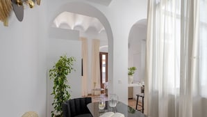 En moderne stue med en sort sofa, et glasbord og en stor stueplante.