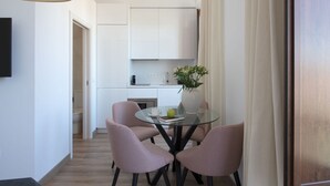Een ruimtelijke leefruimte met een kitchenette, een eethoek met een glazen tafel en geruit gestreept stoelen, en een groot raam met gordijnen.