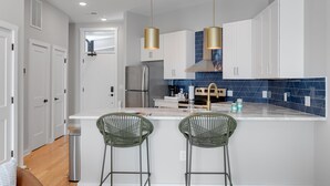 A modern kitchen with white cabinets, a blue backsplash, and two green bar stools.
