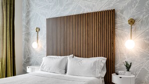 A modern hotel room with a wooden headboard, white bedding, and a small bedside table with a plant.