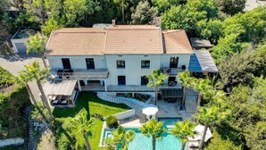 Un'ampia casa a due piani con tetto in tegole, piscina e un giardino curato con palme.