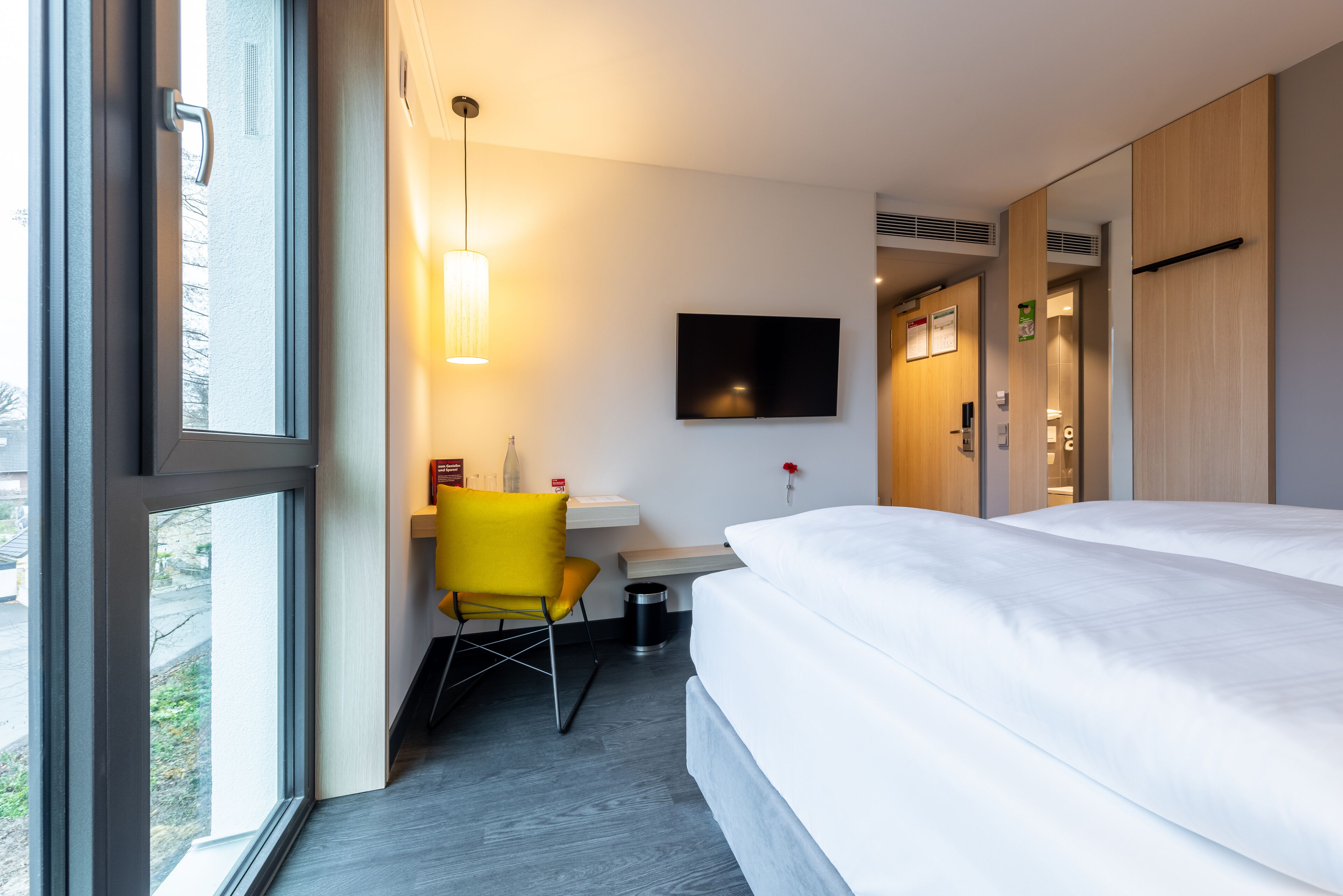 Une chambre d’hôtel avec un lit, un bureau, une chaise, une télévision et une fenêtre.