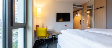 Une chambre d’hôtel avec un lit, un bureau, une chaise, une télévision et une fenêtre.