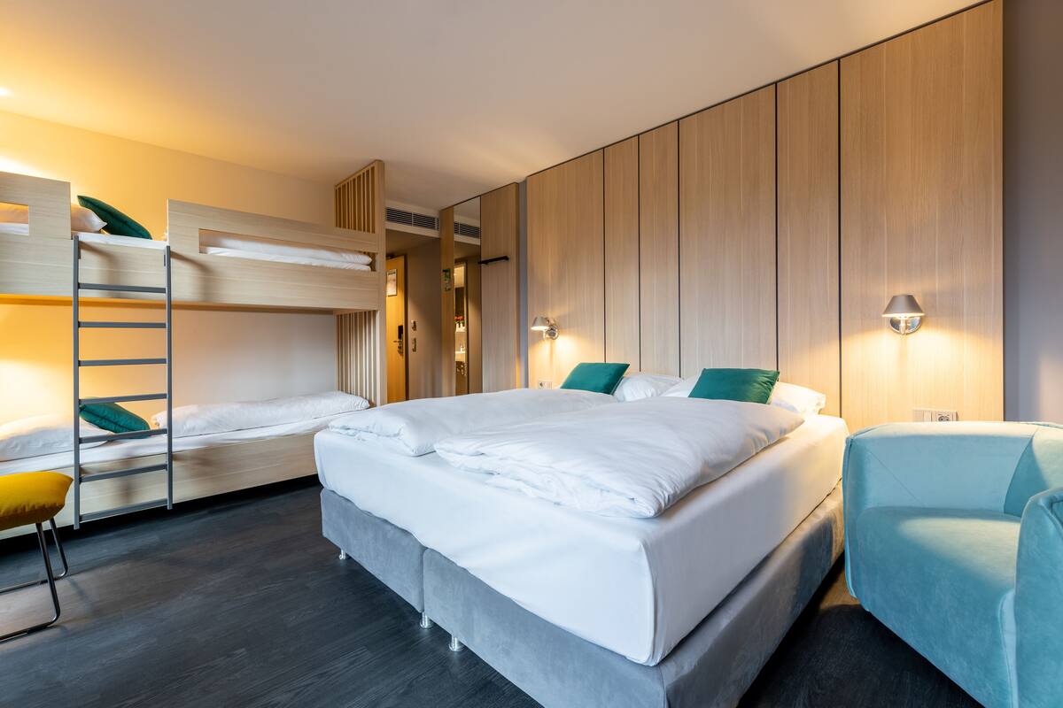 A modern hotel room with a large bed, a bunk bed, a desk, and a chair.