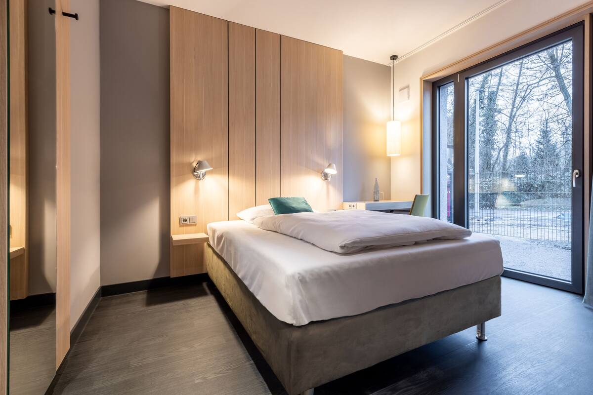 A modern bedroom with a large bed, wooden wardrobe, and a sliding glass door to a balcony.