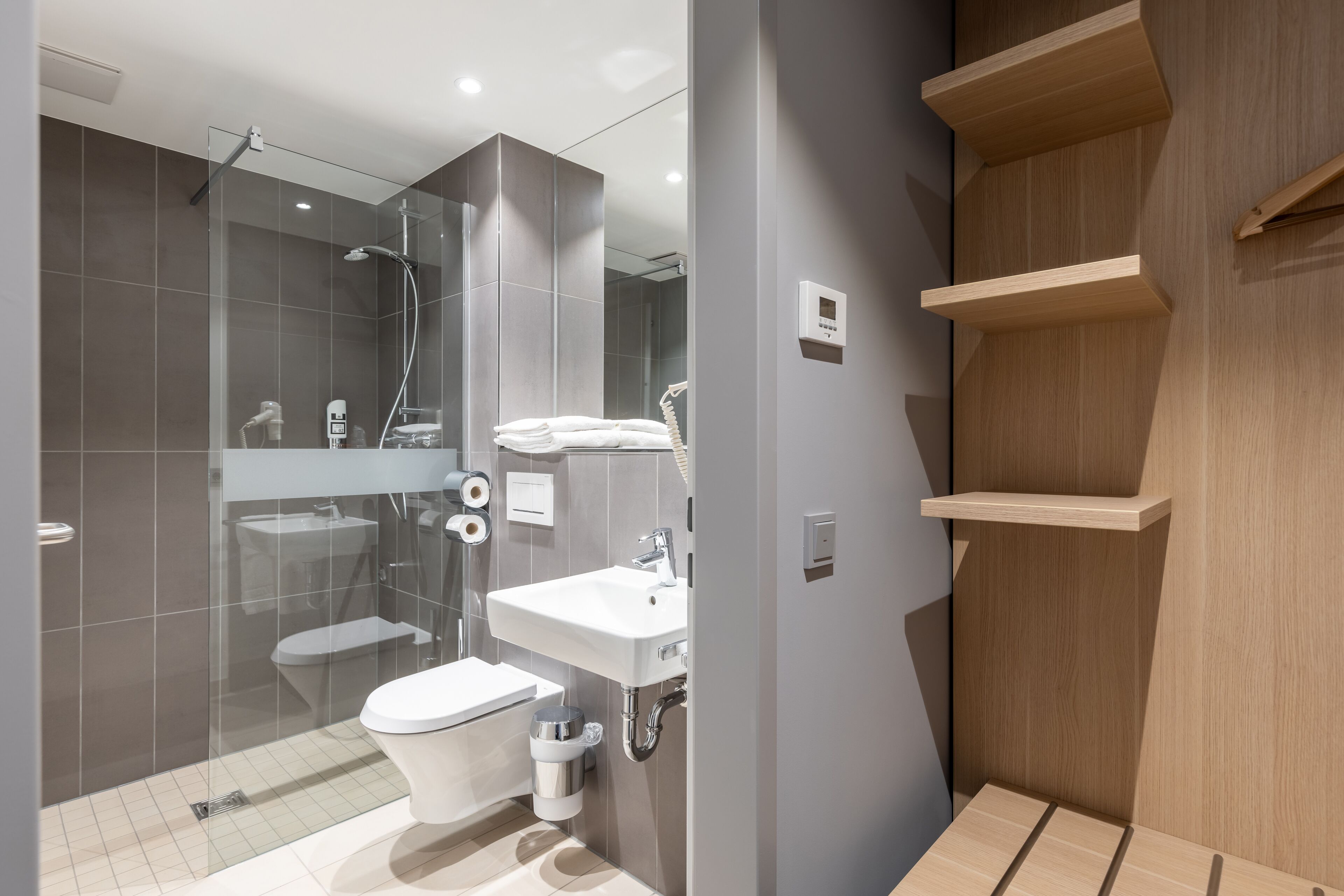 Un baño moderno con ducha de vidrio, un lavabo blanco y un inodoro.