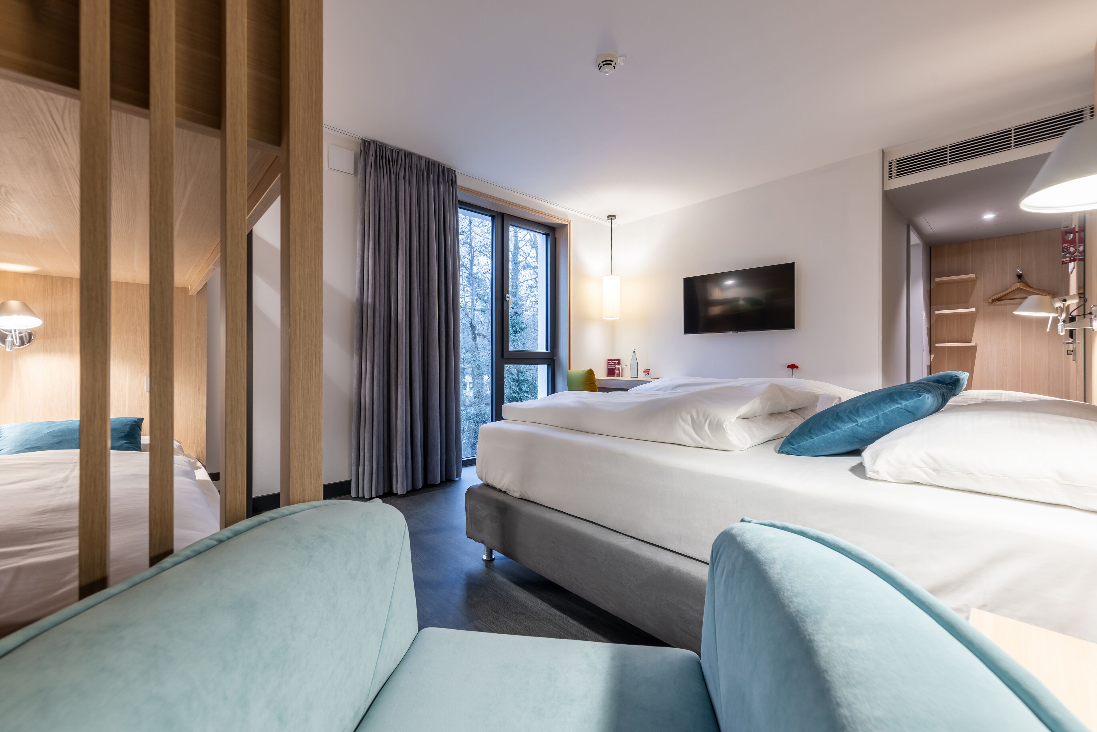 Habitación de hotel con dos camas, televisión, escritorio y ventana con cortinas.