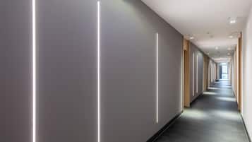 En modern hall med vertikala ljuslister på väggarna, träpanel på höger sida och en lång, rak korridor som leder till en ljusare del av huset.