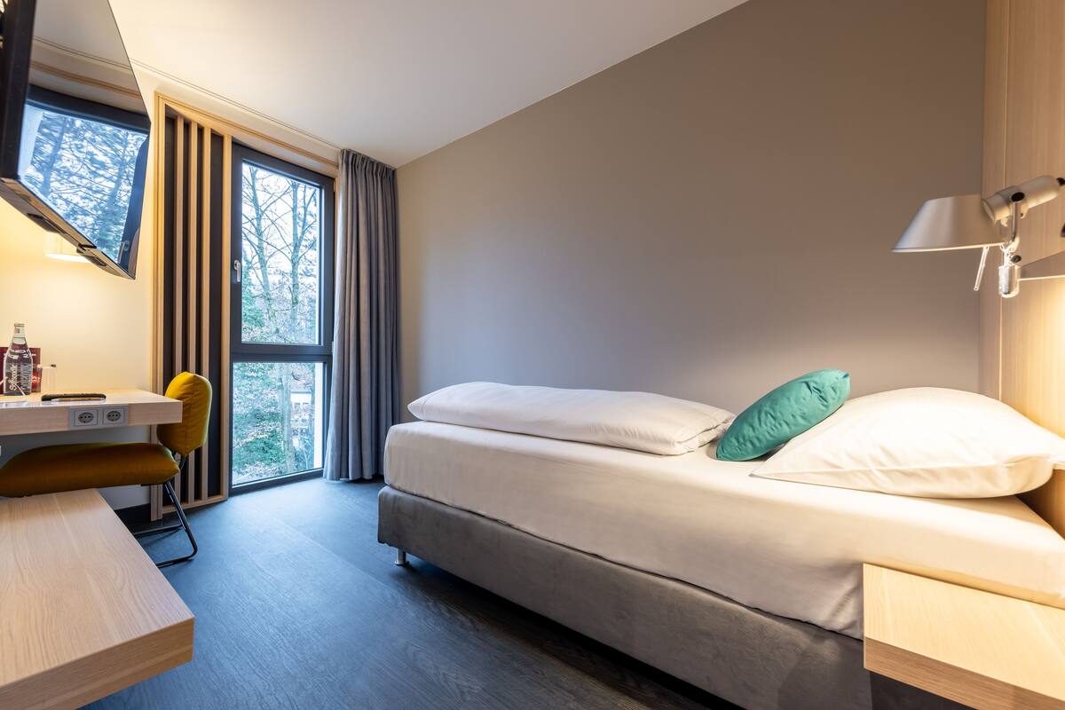A modern hotel room with a bed, a desk, and a chair.
