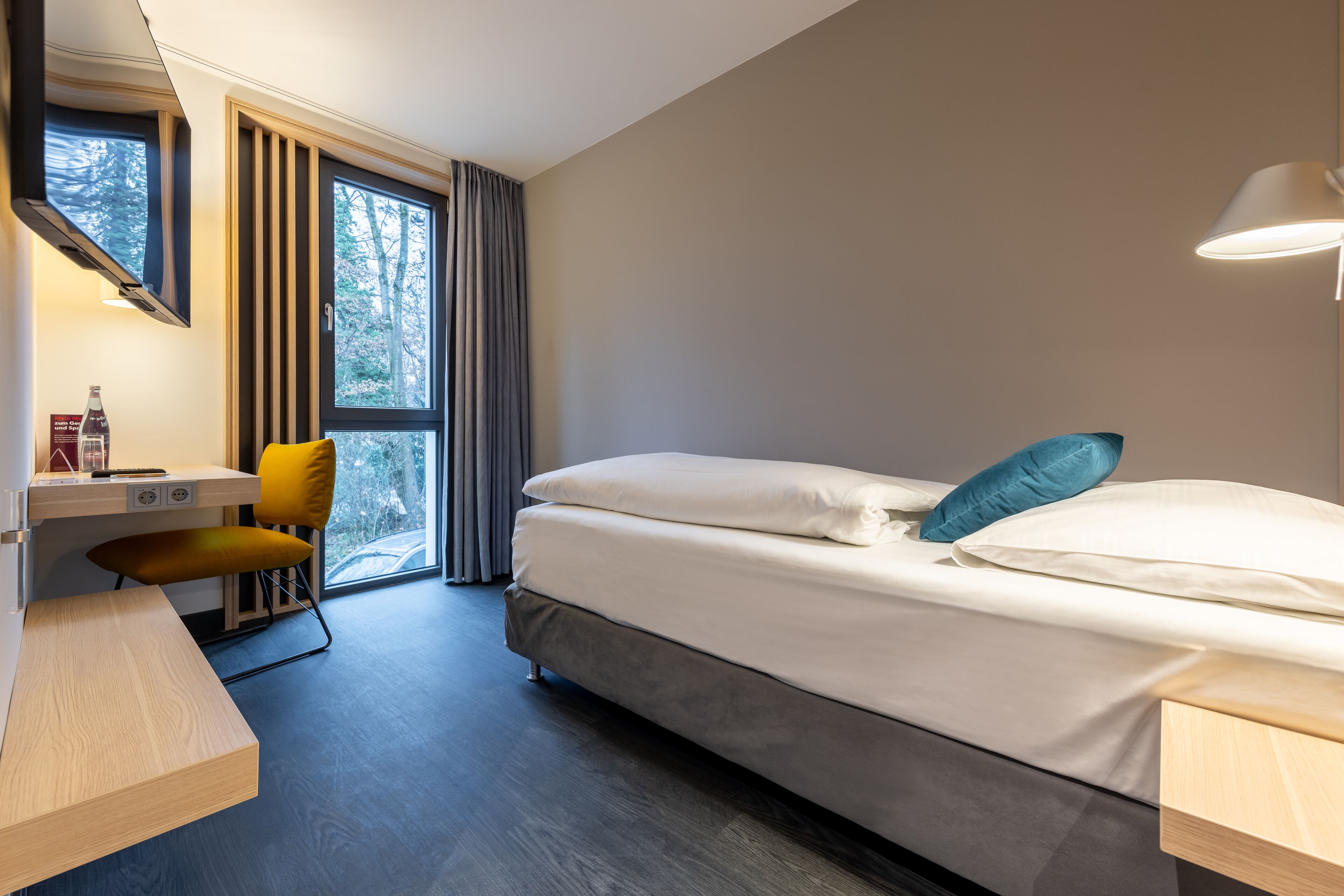 Una habitación de hotel con cama, escritorio, silla y ventana con cortinas.