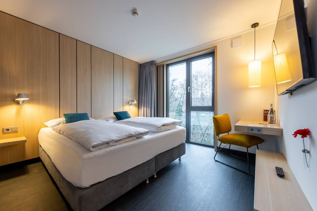 A modern hotel room with a large bed, bedside tables, a desk, and a chair.