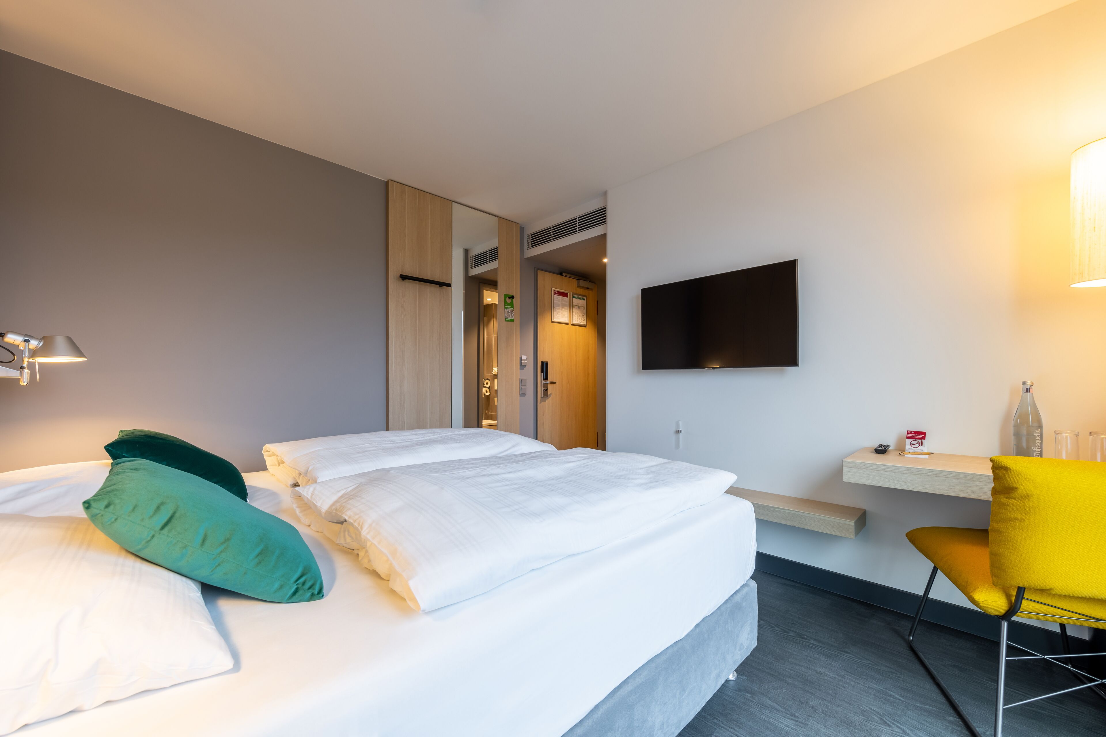 A hotel room with a bed, a desk, a chair, and a TV on the wall.