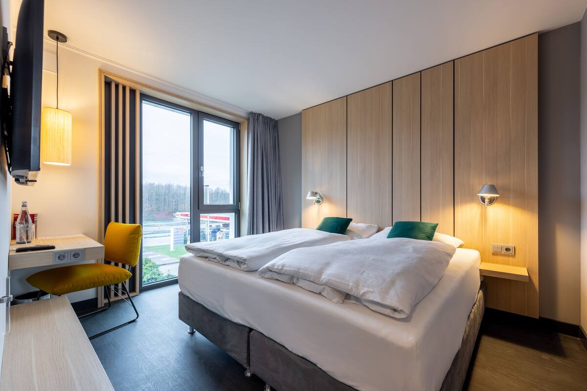 A hotel room with a bed, a desk, a chair, and a TV.