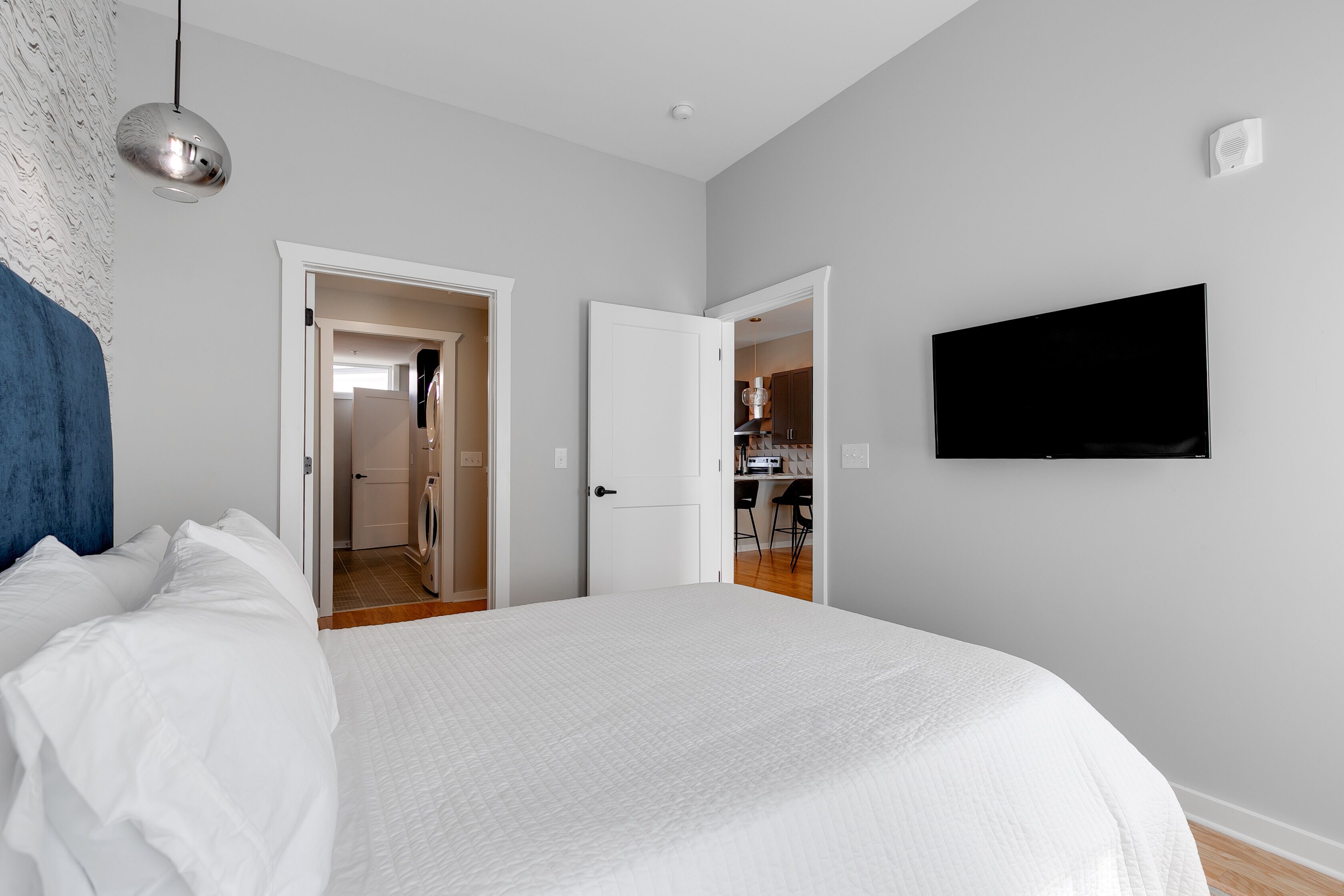 Une chambre avec un grand lit, un téléviseur fixé au mur et une porte donnant sur une salle de bain.