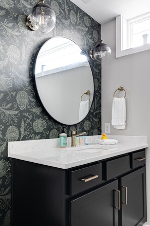 A bathroom with a black vanity, a round mirror, and a white countertop.