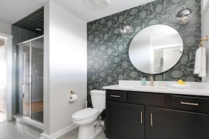 A bathroom with a toilet, a sink with a mirror, and a shower area.