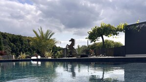 A clear swimming pool with a decorative horse statue in the background, surrounded by lush greenery and a cloudy sky.