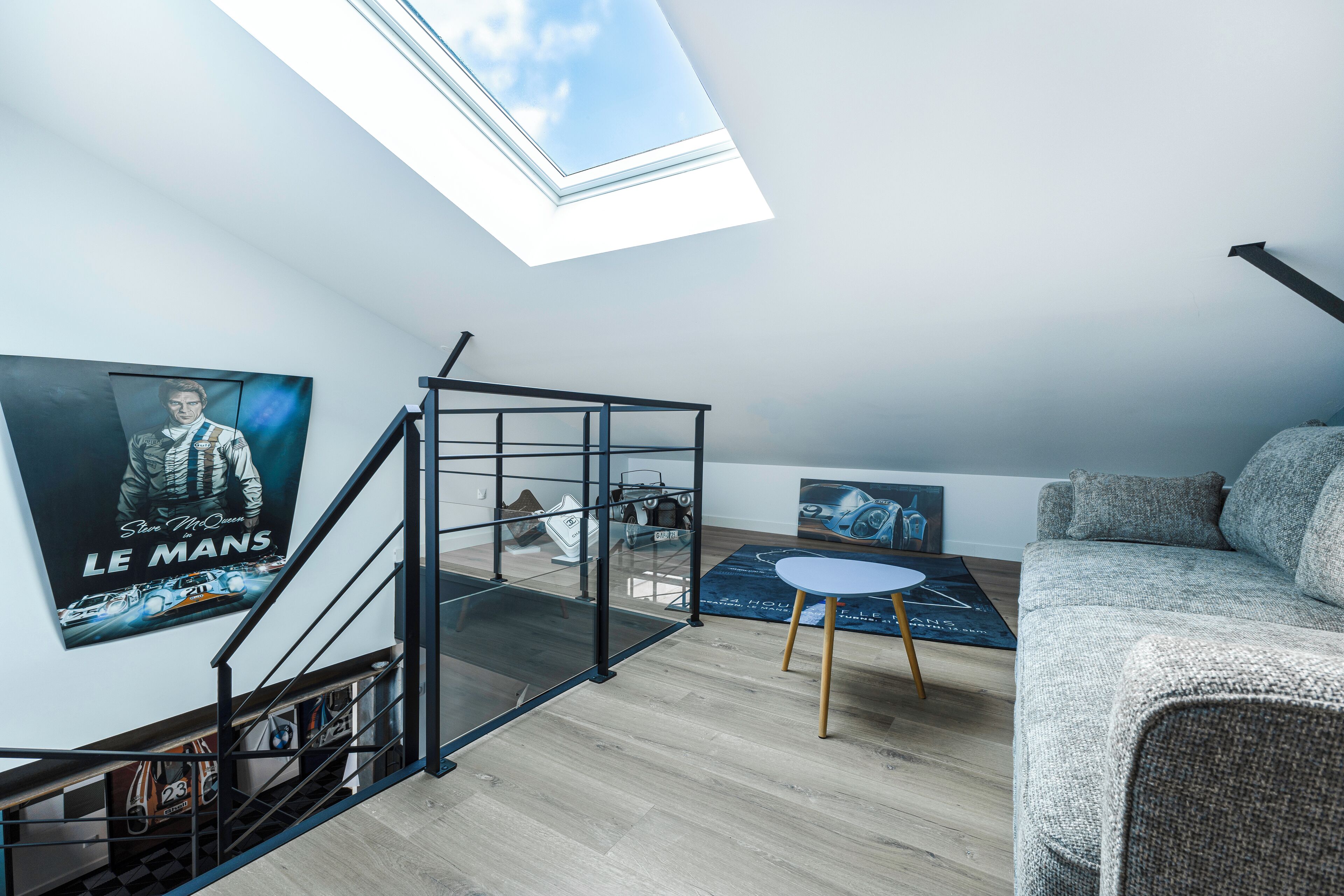 A modern loft with a skylight, a staircase, a sofa, and posters on the walls.