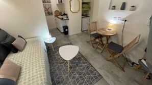 A compact living space with a sofa, a dining table with chairs, a small kitchen area, and a decorative mirror.