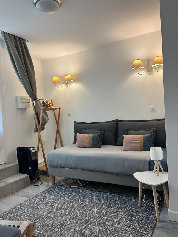 A modern bedroom with a bed, bedside lamps, a radiator, a small table, and a patterned rug.