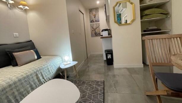 A modern hotel room with a bed, a small table, a chair, a wardrobe, and a mirror.