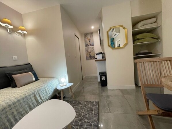 A modern hotel room with a bed, a small table, a chair, a wardrobe, and a mirror.