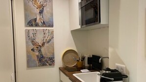 A compact kitchen with a microwave, a sink, and a small trash bin. There are two wall-mounted paintings of deer.
