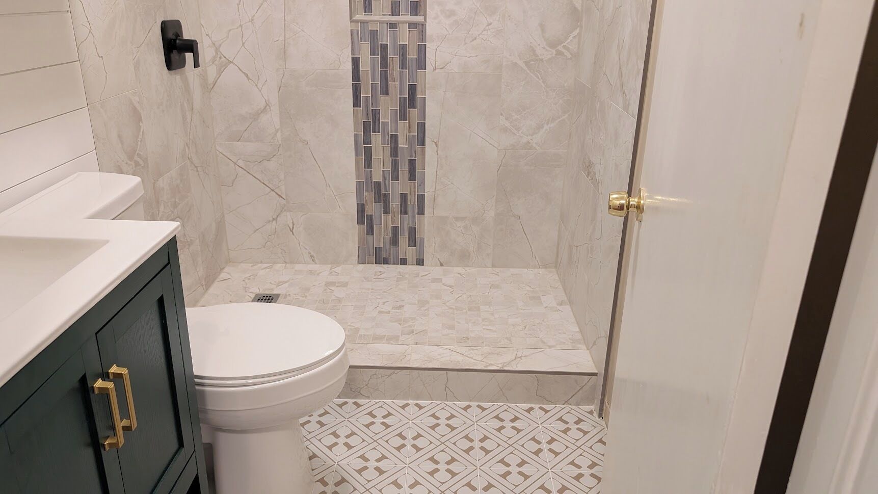 Een badkamer met toilet, een douchegedeelte met betegelde wand en een vloer met patroon.