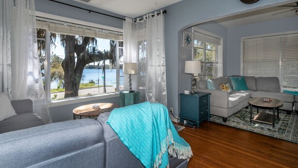 A living room with a sofa, a coffee table, and a side table. There is a window with curtains and a view of a tree and water outside.