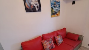 En röd soffa med mönstrade kuddar, en målning av en häst och en annan målning av ett landskap.