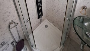 En dusch utan tröskel med en glasdörr, en svart kontrollpanel och ett handfat i glas med en flaska.