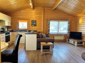 A cozy cabin interior with a kitchen, dining area, and living room, featuring wooden walls and a sloped ceiling.