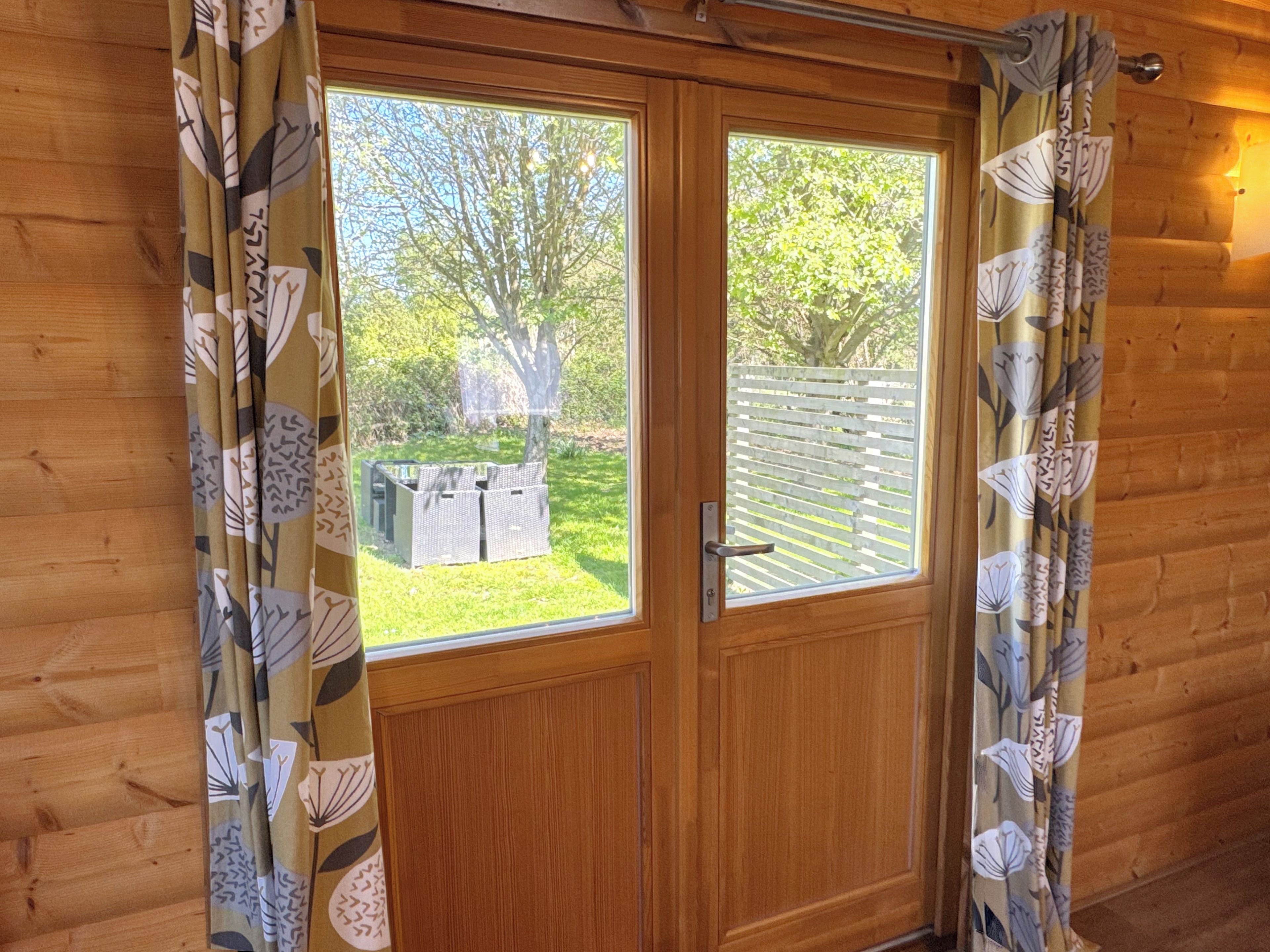 A wooden door with a window, curtains with a leaf pattern, and a view of a garden with a table and chairs.
