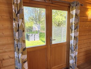 A wooden door with a window, curtains with a leaf pattern, and a view of a garden with a table and chairs.